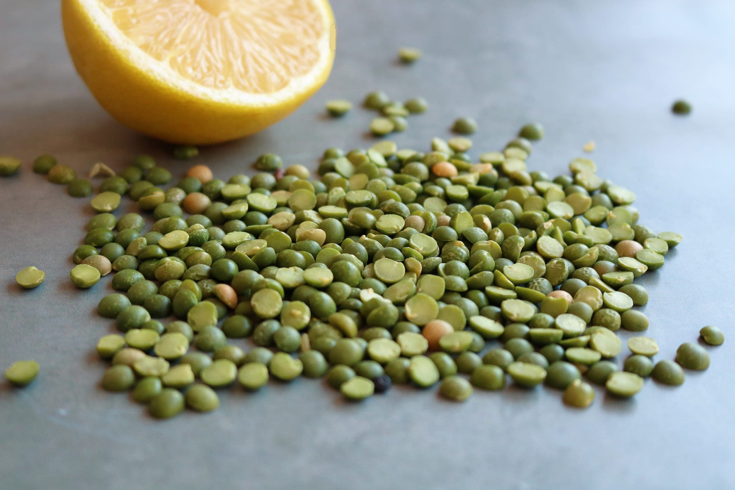 Dried green split peas scattered on a grey surface beside a halved lemon